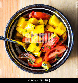 Mango e salsa di pomodoro o insalata con la menta chimichurri in un bianco e nero ciotola su una pineta di sfondo, shot flat-lay. Foto Stock