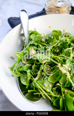 Una semplice insalata verde di mizuna e minatore della lattuga servita con il rabarbaro e semi di papavero condimento, servito in una tazza bianca con un cucchiaio. Foto Stock