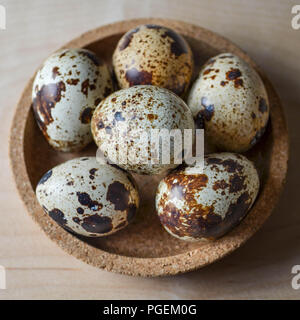 Uova di quaglia comune (Coturnix coturnix) in una piccola ciotola di sughero su uno sfondo di legno. Foto Stock