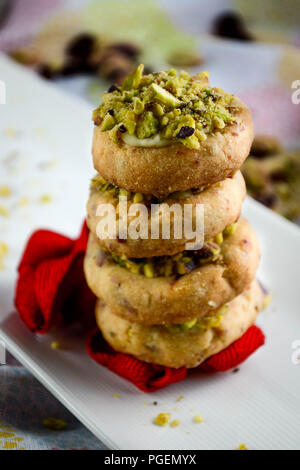 Miniatura di mirtillo palustre di biscotti frollini con cioccolato bianco e pistacchi servita su un piatto e decorate con un nastro rosso Foto Stock