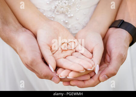 Primo piano due golden fedi sulle palme di sposo e sposa Foto Stock