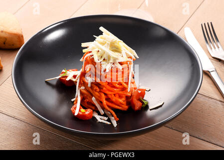 Gli spaghetti in un pomodoro base di pomodoro condito con parmigiano grattugiato e servite in un piatto nero in un angolo alto vista ravvicinata Foto Stock