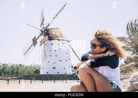 Ricci bella signora seduta rilassante e con sind nei capelli e un mulino a vento sullo sfondo. lato paese luogo scenico per la pace e il relax conce Foto Stock