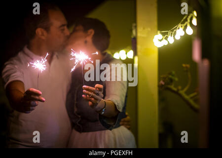 Kissing matura in amore durante una festa a casa celebrando con bagliori di luce. la tenerezza e la felicità per sempre concept focus sul fuoco e uomo e wom Foto Stock