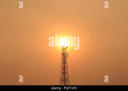 Una torre di telefoni cellulari solitaria si erge in alto sullo sfondo del sole che tramonta. Foto Stock