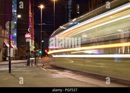 Esposizione lunga scena notturna a Manchester in Inghilterra. Tram Metrolink sentieri di luce. Fotografia della città di notte. Foto Stock