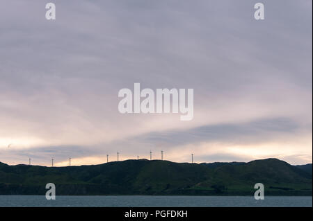 Le turbine eoliche stand stagliano sulla cima di una collina a Cape Terewhiti, Nuova Zelanda. Vista panoramica con bella alba sky. Foto Stock