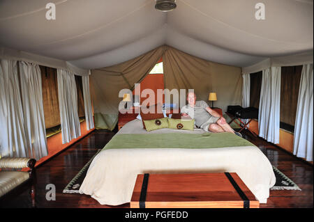 L'uomo rilassarsi all'interno di una tenda di lusso in un safari campeggio, il Masai Mara, Kenya, Africa. Foto Stock