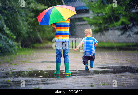 Bambini passeggiate in wellies in una pozza sul tempo piovoso Foto Stock