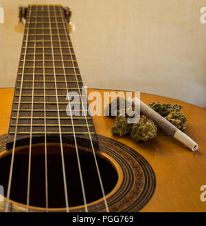 Tastiera e collo di una classica o chitarra spagnola con la marijuana gemme e giunto su di esso. Sfondo bianco con effetto di sfocatura. Vista ravvicinata. Foto Stock