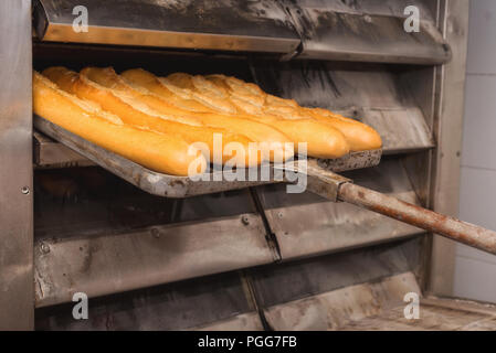 Baker tenendo fuori pane fresco dal forno industriale Foto Stock