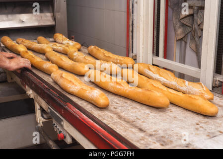 Baker tenendo fuori pane fresco dal forno industriale Foto Stock