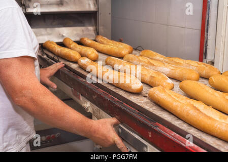 Baker tenendo fuori pane fresco dal forno industriale Foto Stock