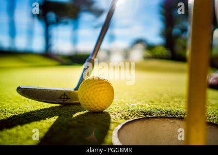 Mini Golf sfera gialla con un bat in prossimità del foro al tramonto Foto Stock