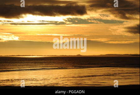 Cielo all'alba dalle tempeste scure sopra il Castello di Bamburgh, Northumberland, visto all'orizzonte oltre la strada rialzata fino a Holy Island. Preso da Berwick su Tweed Foto Stock