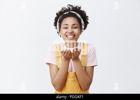 Raccogliere tutti la mia speranza e il mio amore di palme, dando a voi. Ritratto di affascinante gioiosa americano africano nella fascia e tute da elegante, tenendo le mani insieme come libro vicino al petto e sorridente largamente Foto Stock