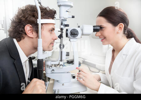 Un uomo avente un occhio test con lampada a fessura / medico donna in Oftalmologia Clinica facendo retina cornea diagnostica esame con la visione del paziente dalla moderna c Foto Stock