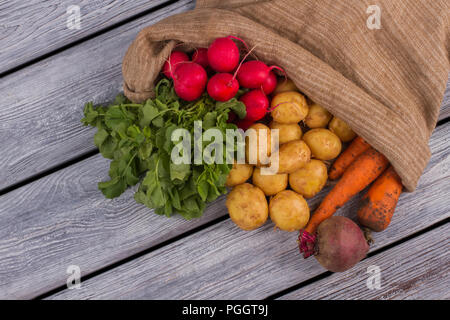 Borsa di tela con vari ortaggi su legno. Prezzemolo, Rafano, patate, carote e barbabietole. Grigio backgorund di legno. Foto Stock