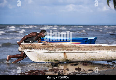 Fisherman spingendo la sua barca fuori dell'oceano in Livinston, Guatemala Foto Stock