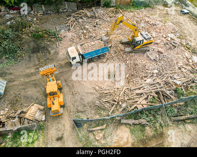 Vista aerea di macchinari pesanti costruzione. escavatore carico di un autocarro con pianale di scarico dopo la demolizione di casa Foto Stock