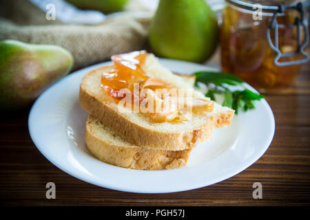 Pezzi di pane con dolci fatti in casa a base di marmellata di frutta da pere e mele in un piatto su un tavolo di legno Foto Stock