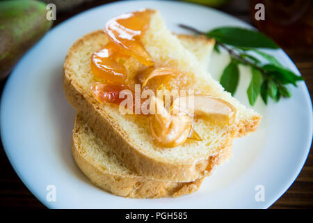 Pezzi di pane con dolci fatti in casa a base di marmellata di frutta da pere e mele in un piatto su un tavolo di legno Foto Stock