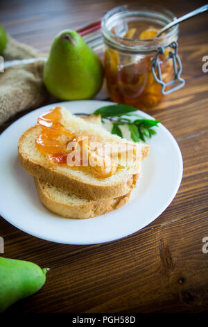 Pezzi di pane con dolci fatti in casa a base di marmellata di frutta da pere e mele in un piatto su un tavolo di legno Foto Stock