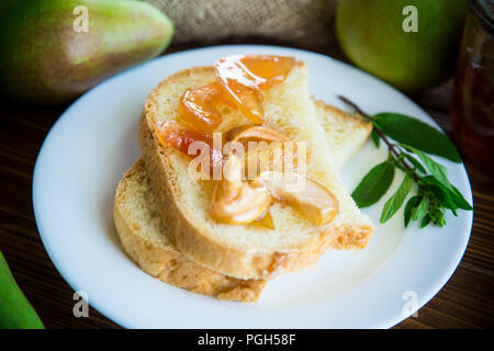 Pezzi di pane con dolci fatti in casa a base di marmellata di frutta da pere e mele in un piatto su un tavolo di legno Foto Stock