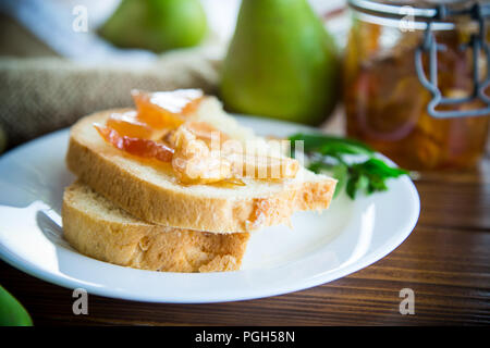 Pezzi di pane con dolci fatti in casa a base di marmellata di frutta da pere e mele in un piatto su un tavolo di legno Foto Stock