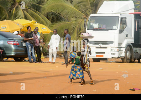 OUIDAH, BENIN - Jan 10, 2017: Unidentified Beninese donna con bacinella sul suo capo passeggiate con i suoi figli al mercato locale. Benin di persone soffrono di p Foto Stock