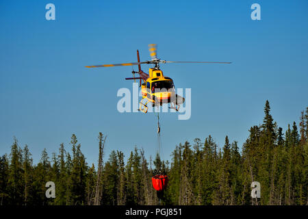 Un'immagine orizzontale di un elicottero giallo portante una benna caricata con acqua per un incendio di foresta nelle zone rurali di Alberta in Canada. Foto Stock