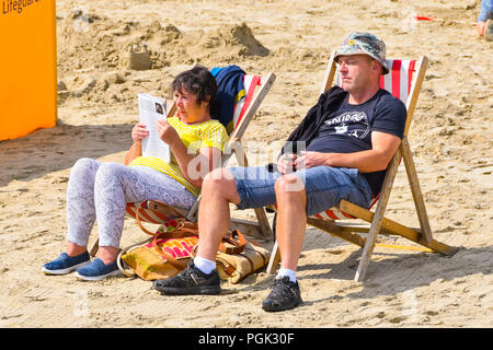 Lyme Regis, Dorset, Regno Unito. Il 27 agosto 2018. Regno Unito Meteo. Un paio di godersi il caldo le magie di sole sulla spiaggia presso la località balneare di Lyme Regis in Dorset su Bank Holiday lunedì dopo la domenica era un washout. Credito Foto: Graham Hunt/Alamy Live News Foto Stock