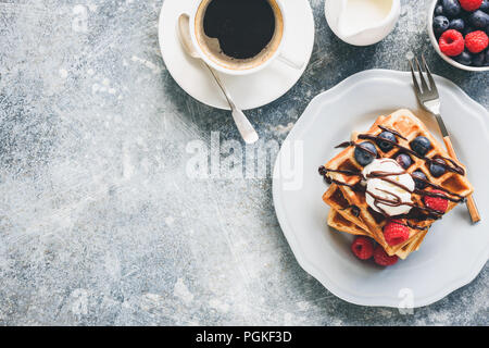 Cialde belghe con gelato, bacche e la tazza di caffè sul cemento dello sfondo. Vista da sopra con copia spazio per il tuo testo. Una gustosa prima colazione Foto Stock