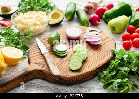 Ortaggi freschi sul bordo di taglio. Il cetriolo, la cipolla, peperoncino, prezzemolo, il ravanello di avocado bulgur preparazione di insalata Foto Stock