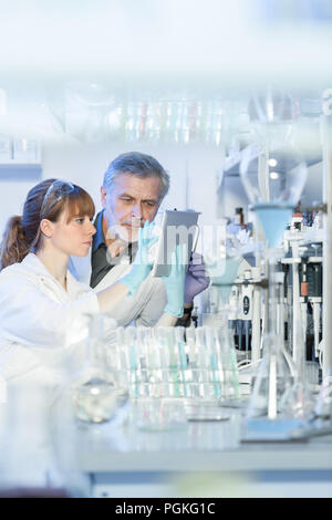Health care i ricercatori impegnati nella vita laboratorio scientifico. Giovani donne scienziato e senior supervisore maschio cercando focalizzati a tablet co Foto Stock