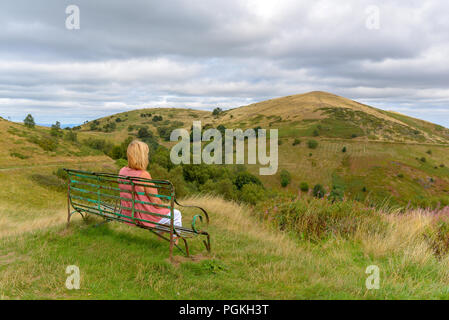 Donna seduta su una panchina affacciato sulla collina nord, Malvern Hills, Worcestershire, England, Regno Unito Foto Stock