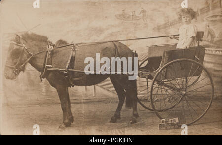 L'annata 1923 Studio fotografia di un giovane ragazzo chiamato Raymond in sella a un asino Carrello a Southend-On-Mare, Essex, Inghilterra Foto Stock