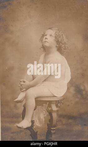 Vintage fotografia di una bionda dai capelli ricci bambino seduto su un piedistallo che indossa una toga (Cherubino immagine) Foto Stock