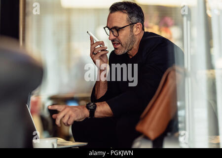 Imprenditore maturo parlando al telefono mentre guardando il laptop. CEO lavorare stando seduti nella hall degli hotel. Foto Stock