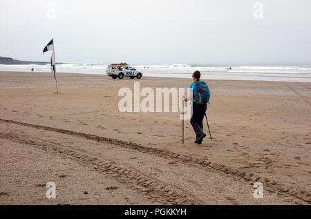 Lone Donna che cammina in Croyde Bay con bagnino RNLI veicolo parcheggiato sulla spiaggia a sud ovest percorso costiero, Devon, Inghilterra, Regno Unito. Foto Stock