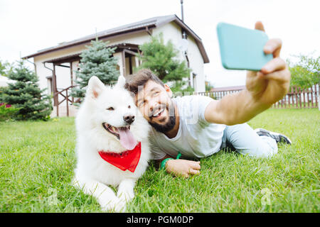 Uomo e husky sdraiati sull'erba vicino casa estiva facendo foto Foto Stock