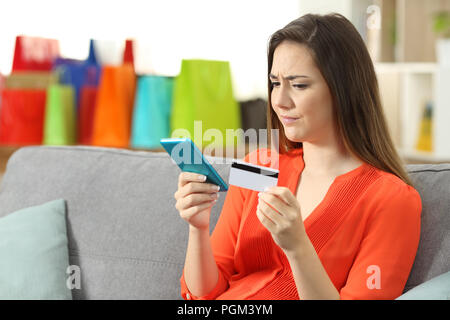 Confuso donna pagare online con una carta di credito seduta su un divano nel salotto di casa Foto Stock