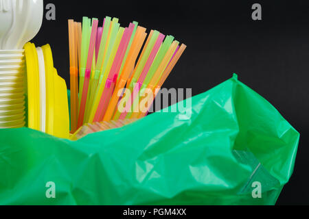 Primo piano di colorati dei rifiuti di plastica nel verde di un sacco per rifiuti riciclabili come uso singola posate inquinamento concetto indesiderata isolati su sfondo nero Foto Stock