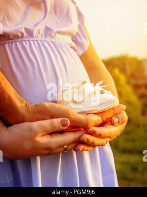 Close-up della donna incinta, ventre con scarpe per bambini, concetto di incantevole futuri genitori Foto Stock