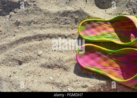 Pantofole da donna rosa con divorzi verdi e gialli su sabbia gialla con la spiaggia poco profonda del Mar Nero nel pomeriggio. Foto Stock