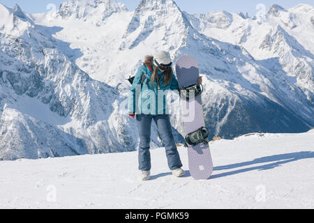 Snowboarder ragazza sullo sfondo delle montagne nella stagione invernale si gode il panorama. Concetto di snowboard, lifestyle, sport, avventura. Foto Stock
