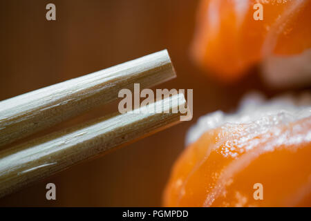 Usa e getta bacchette di bambù e salmone sushi di ripresa macro su sfondo di legno Foto Stock