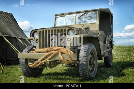 Una vecchia Jeep Willys parcheggiata in un campo accanto a una tenda Foto Stock