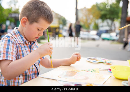 Carino piccolo ragazzo di disegno con vernici colorate in autunno park. Creative pittura per bambini sulla natura. Attività all'aperto per il toddler kid. Talento dolore dei bimbi Foto Stock