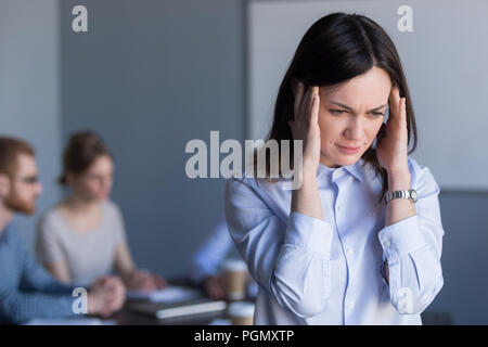 Sottolineato lavoratore di sesso femminile che soffrono di mal di testa durante la carica meetin Foto Stock